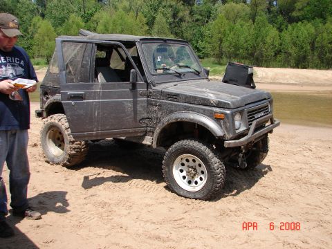 1987 Ford Bronco - A Suzuki Samurai is parked on a sandy area with trees in the background. The date "APR 6 2008" is visible.