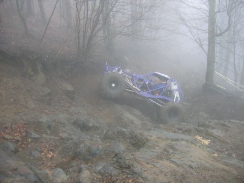 1992 Ford Mustang - An off-road buggy navigates a challenging, muddy incline amidst a foggy forest landscape.