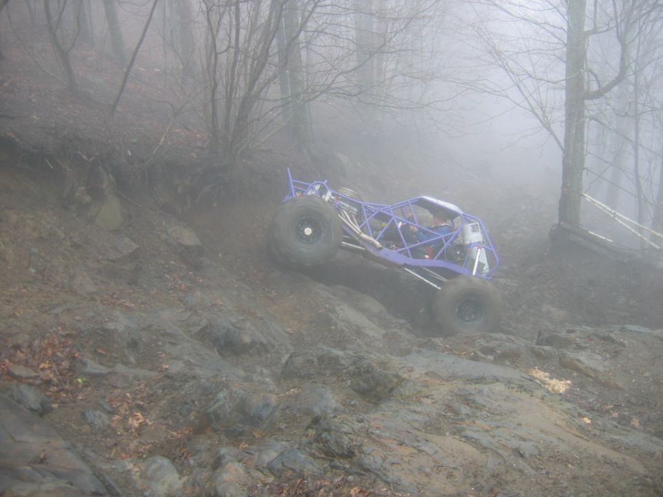 Purple off-road buggy climbing a muddy, rocky hill in foggy woods