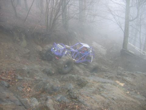 1992 Ford Mustang - Off-road buggy navigates a challenging muddy and rocky slope in foggy conditions.