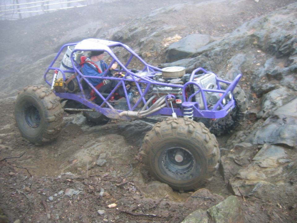 Purple buggy with big tires crawling over rocks and mud. Driver in blue jacket and helmet