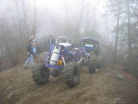 1992 Ford Mustang - Several off-road vehicles and people are gathered on a muddy, wooded trail on a foggy day.