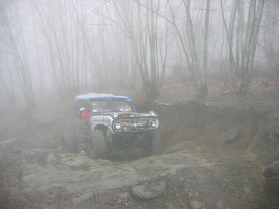 1970s Ford Bronco navigating a rocky, muddy trail in foggy woods