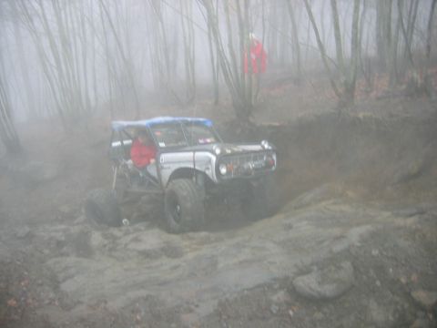 1992 Ford Mustang - Off-road vehicle with roll cage driving through a muddy, wooded area on a foggy day.