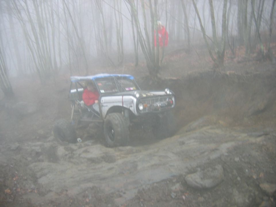 Modified off-road vehicle with roll cage navigating a muddy trail in a foggy forest