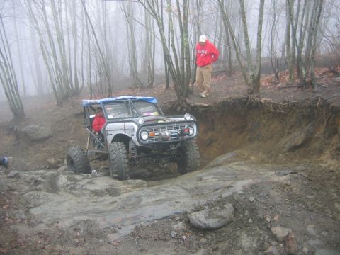 1992 Ford Mustang - A heavily modified off-road vehicle tackles a challenging muddy terrain in a wooded area.