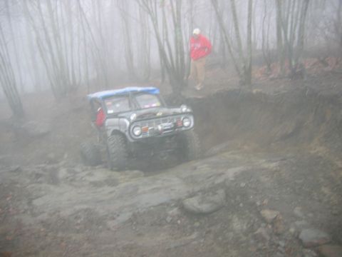 1992 Ford Mustang - An off-road vehicle navigates a challenging muddy and rocky path through a foggy forest.