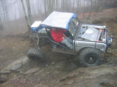 1992 Ford Mustang - Modified Ford Bronco navigating a challenging off-road trail in foggy, wooded terrain.
