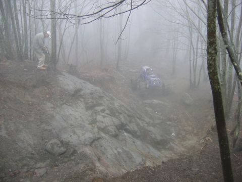 1992 Ford Mustang - A person watches an off-road vehicle descend a treacherous, fog-shrouded slope in a wooded area.