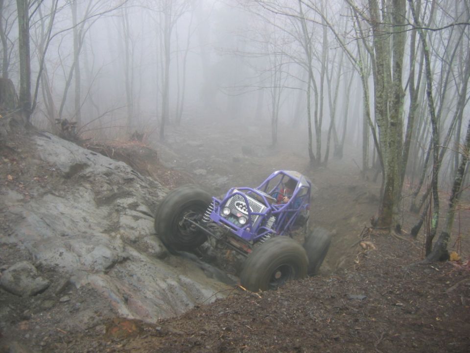 Purple off-road buggy with large tires navigating a muddy, rocky incline in a foggy forest