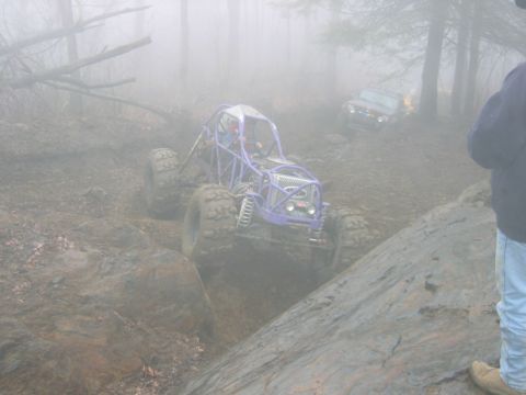 1992 Ford Mustang - An off-road buggy tackles a challenging muddy and rocky course amidst fog, with another vehicle in the background.