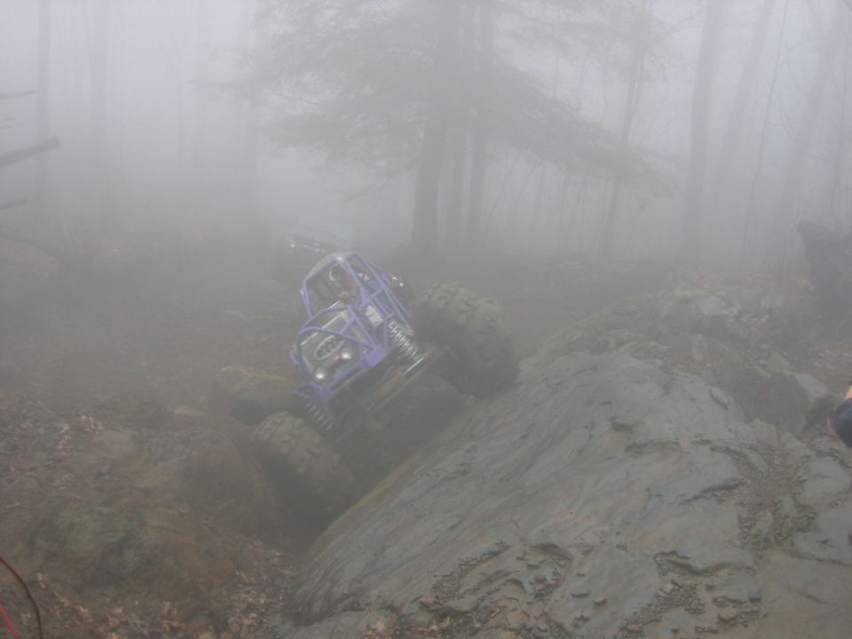 Purple off-road buggy climbing a rocky, muddy hill in foggy woods