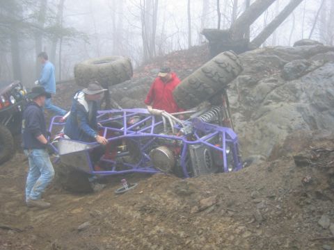 1992 Ford Mustang - An off-road buggy is stuck in the mud on a hill with several people attempting to help.