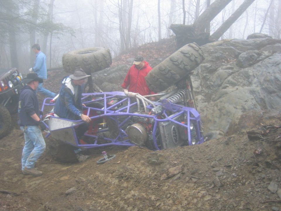 Off-road buggy stuck in mud with people around it; another vehicle visible to the left