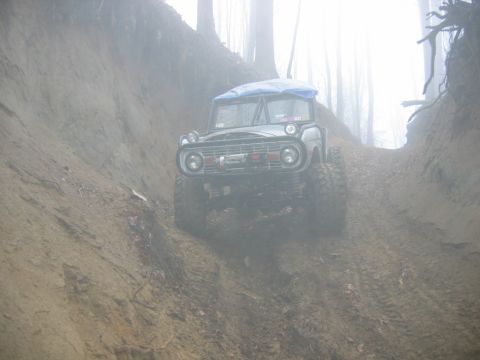 1992 Ford Mustang - An off-road vehicle navigates a steep, muddy hill in a foggy, wooded environment.