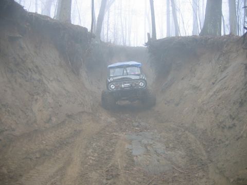 1992 Ford Mustang - A classic Ford Bronco navigates a challenging muddy path through a misty wooded area.