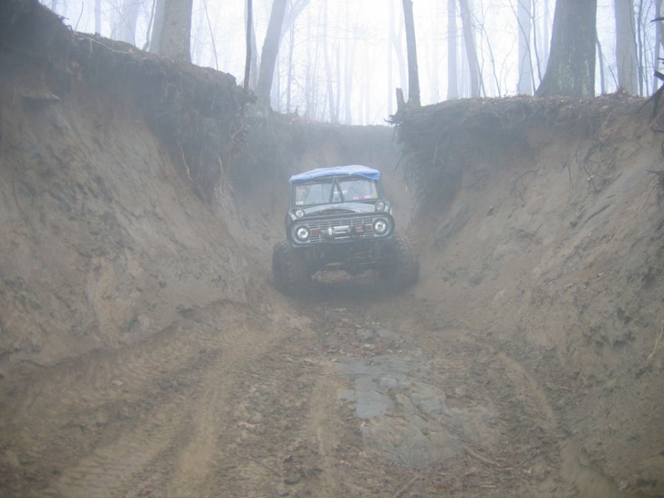Ford Bronco driving down a muddy, steep ravine in a foggy forest