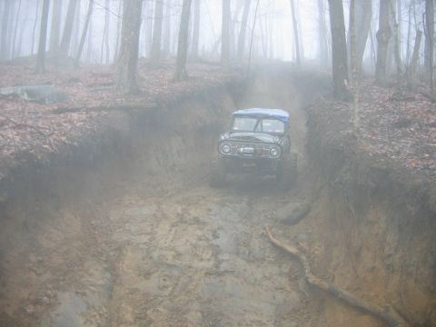 1992 Ford Mustang - An off-road vehicle navigates a challenging muddy path through a misty forest.