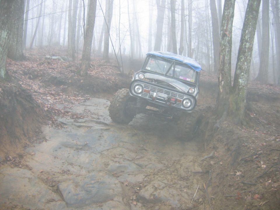 1970s Ford Bronco off-roading on a wet, rocky, and muddy trail in a foggy forest