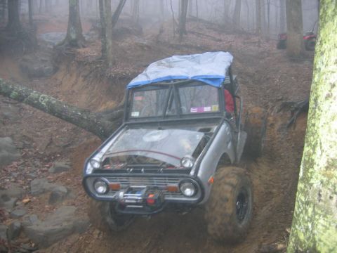 1992 Ford Mustang - An off-road vehicle tackles a challenging muddy terrain in a forest setting, with another vehicle visible in the background.