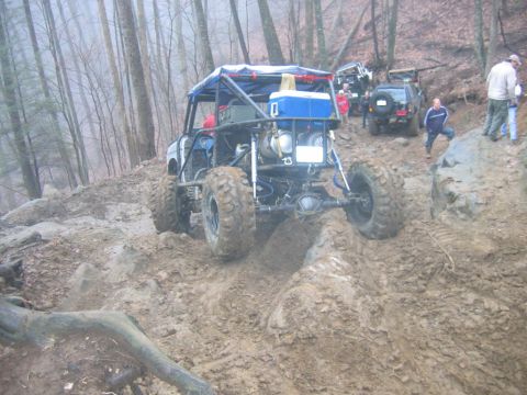 1992 Ford Mustang - Several off-road vehicles navigate a challenging muddy trail in a wooded area.