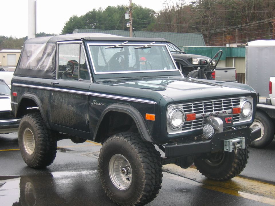 Dark green Ford Bronco with a soft top, lifted suspension, and winch on the front bumper