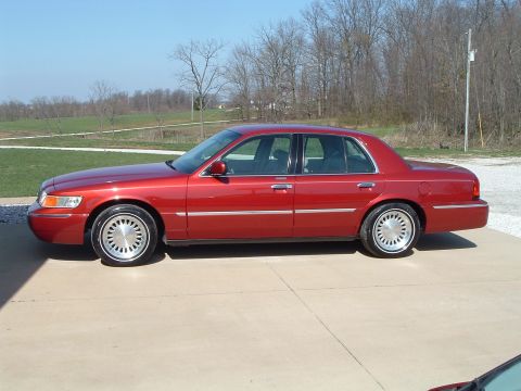 1999 Mercury Grand Marquis - Side view of a red 1999 Mercury Grand Marquis sedan parked on a concrete driveway.