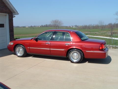 1999 Mercury Grand Marquis - This red sedan is parked on a concrete driveway next to a brick garage on a sunny day.