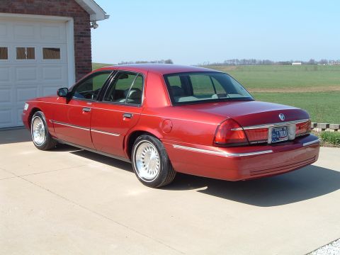 1999 Mercury Grand Marquis - This red sedan is parked in front of a brick garage with a white door.