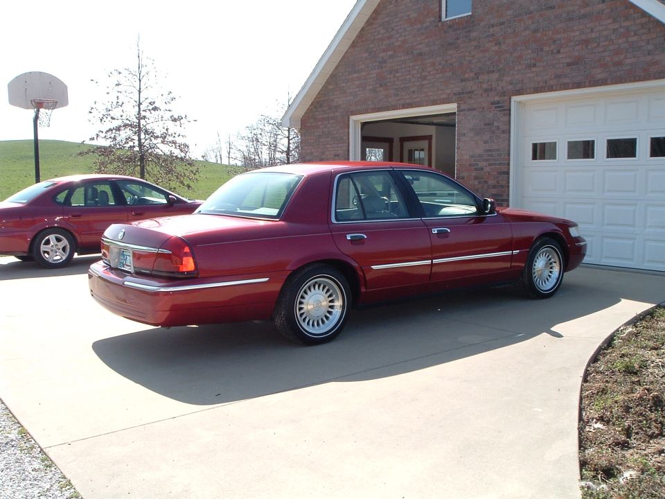 Red 1999 Mercury Grand Marquis parked in driveway next to another red sedan