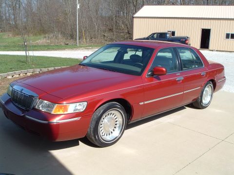 1999 Mercury Grand Marquis - A red sedan is parked outside a building, with a pickup truck visible behind it.