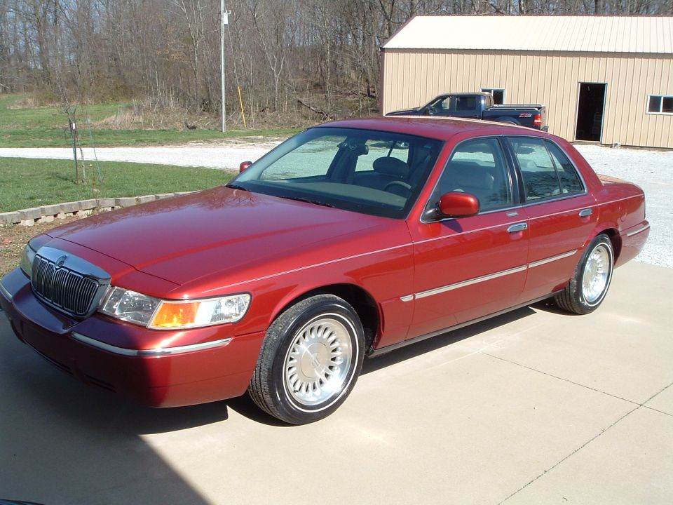 Red sedan parked on concrete, with a dark pickup truck in the background