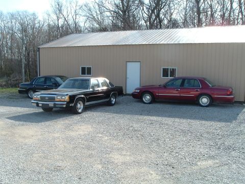 1999 Mercury Grand Marquis - Three sedans are parked outside a building. The maroon car on the right is a 1999 Mercury Grand Marquis.
