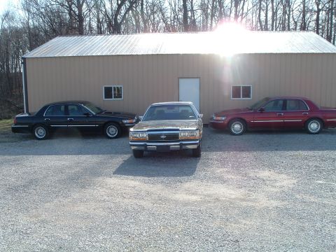 1999 Mercury Grand Marquis - Three sedans are parked in front of a building. The middle car appears to be a Ford Crown Victoria.