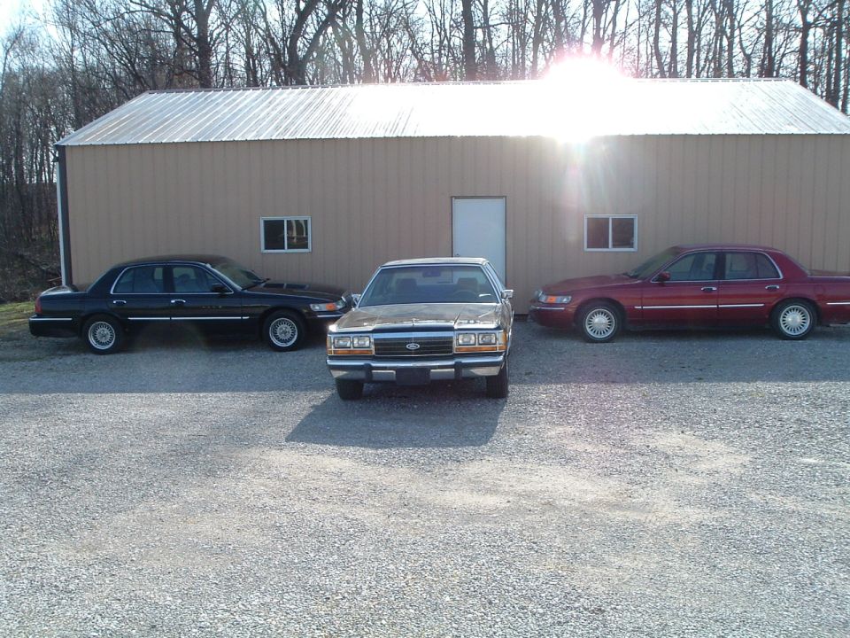 Three sedans parked in front of a tan building. The middle car is gold, the left is black, and the right is red