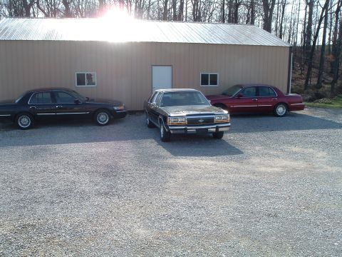 1999 Mercury Grand Marquis - Three sedans are parked in front of a building on a gravel lot.