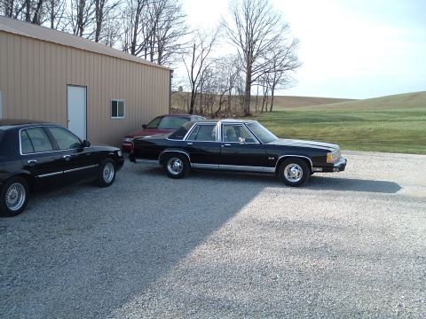 1999 Mercury Grand Marquis - Two black sedans and a red sedan are parked on a gravel lot next to a building.