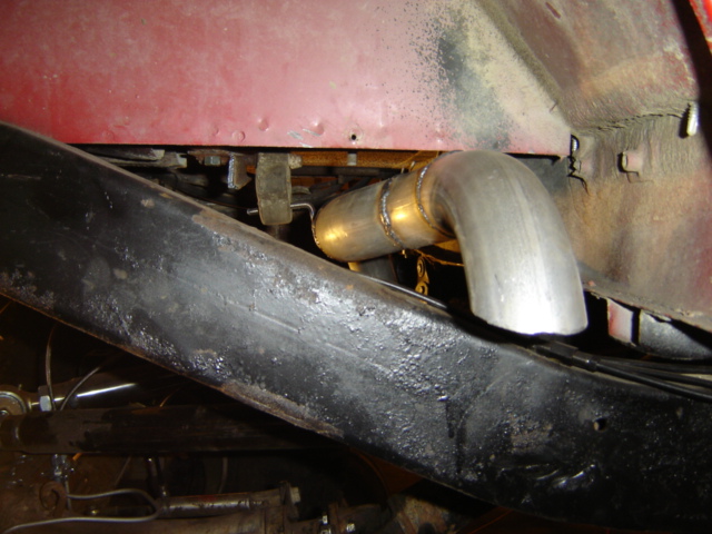 Exhaust pipe bends over black frame rail under red body panel