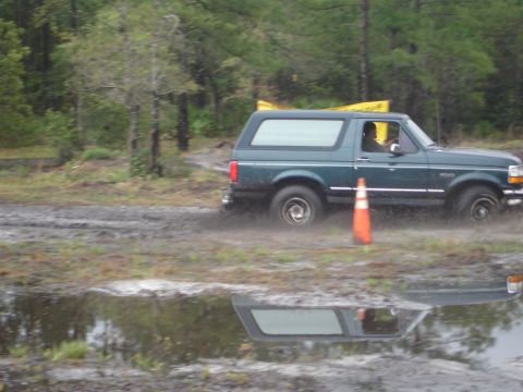 1989 Ford Bronco - A green Ford Bronco navigates a muddy track, kicking up water and dirt.