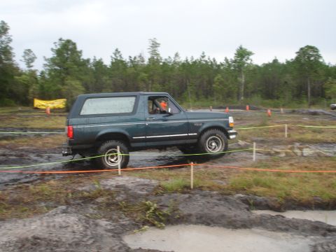 1989 Ford Bronco - A dark green Ford Bronco tackles a muddy obstacle course during an event.