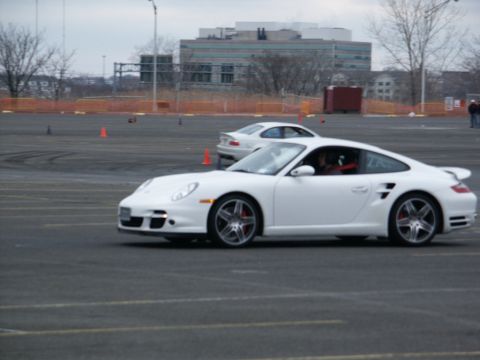 2001 Mercury Grand Marquis - A white Porsche 911 Turbo is seen on a track, with another car in the background and orange cones marking the course.