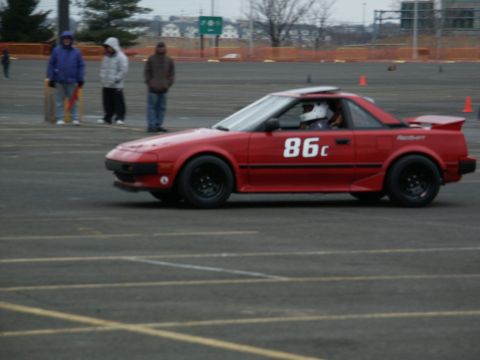 2001 Mercury Grand Marquis - A red sports car with racing number 86c drives on a paved track with orange cones in the background.