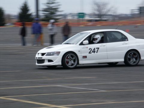 2001 Mercury Grand Marquis - A white Mitsubishi Lancer Evolution with racing number 247 navigates a track, driven by a helmeted individual.