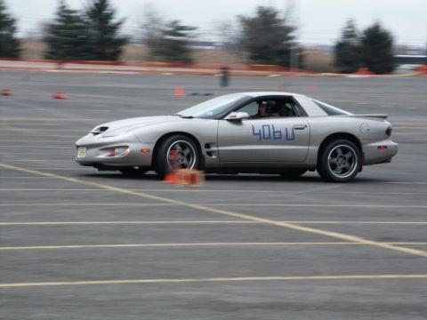 2001 Mercury Grand Marquis - A silver Pontiac Firebird is seen in motion on a paved track, navigating around orange cones.