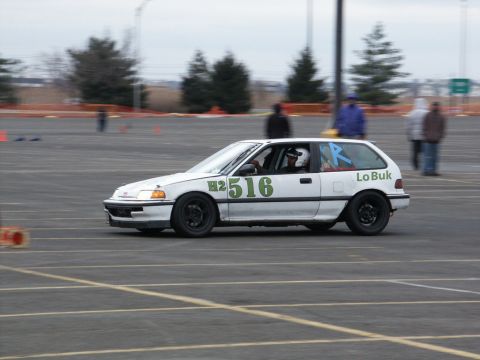 2001 Mercury Grand Marquis - A white hatchback race car with green numbers H2 516 and a blue R on the rear window is seen on a track.