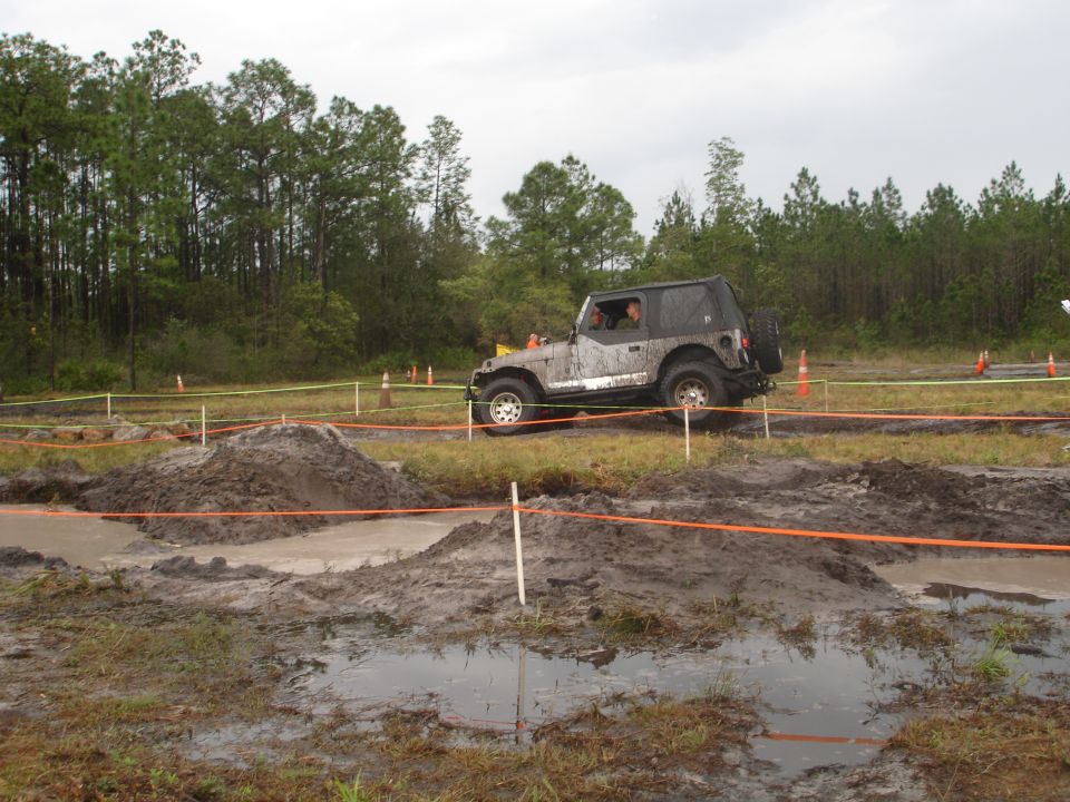 Mud-splattered Jeep Wrangler on an off-road course with orange and yellow caution tape