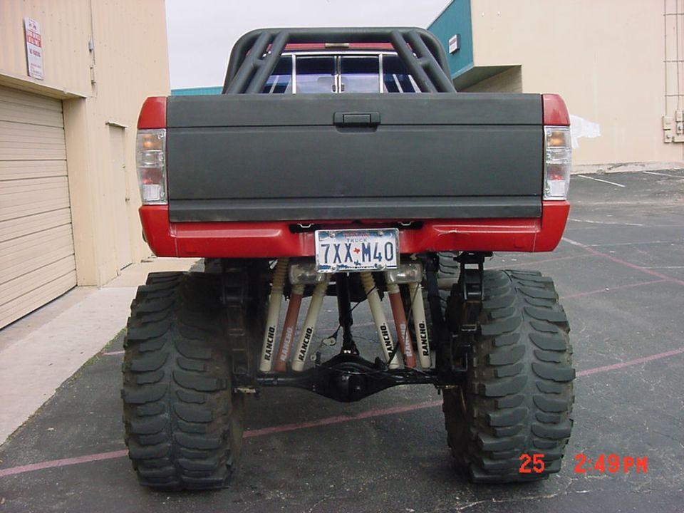 Rear of red lifted mini truck on huge mud tires showing coilover suspension, plate 7XX M40