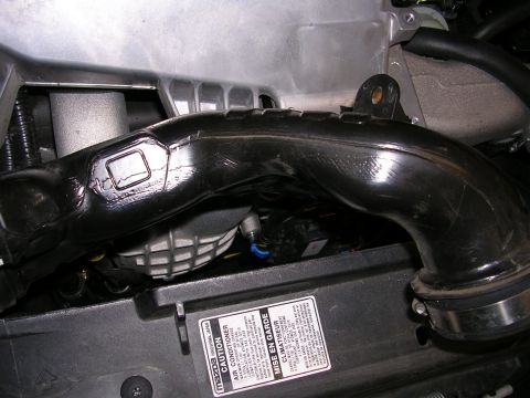 2007 Mazda 3 - Close-up of a black engine intake tube, with a visible Mazda caution sticker indicating the vehicle is a 2007 model.