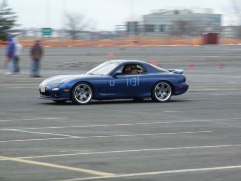 2001 Mercury Grand Marquis - A blue Mazda RX-7 with racing numbers is captured in motion on a track during an event.