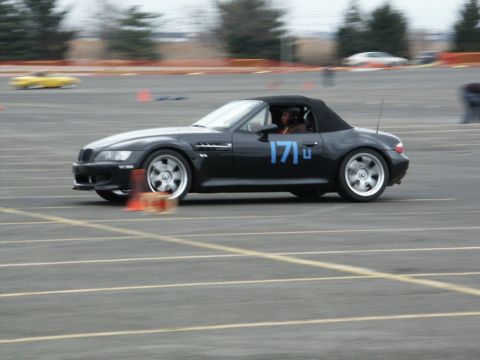 2001 Mercury Grand Marquis - A black convertible sports car with the number 171 on its door navigates a course, with another yellow car blurred in the background.